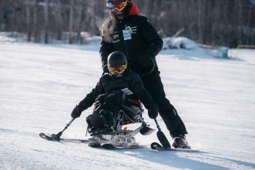 person riding a sit ski with someone behind helping them out