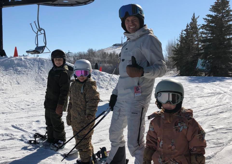 A father stands with his three children, all of them on skis.