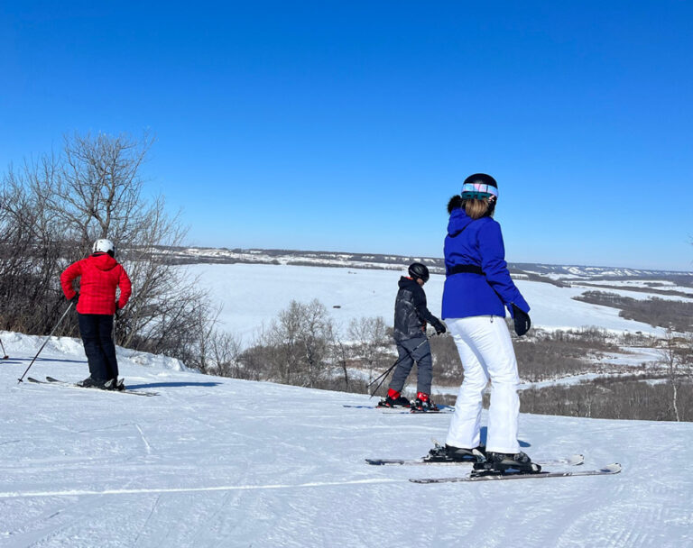 Three skiiers stand atop Asessippi Ski Hill, preparing to head down the hill.