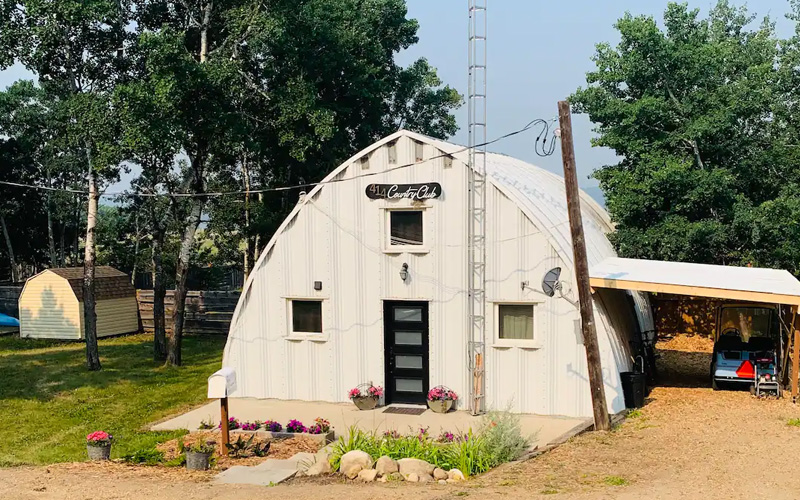 A white, barn shaped structure with a covered parking area attached. Our Cozy Quonset.