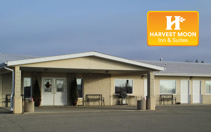 A tan colored motel sits in a parking lot. This motel is the Harvest Moon Inn & Suites.