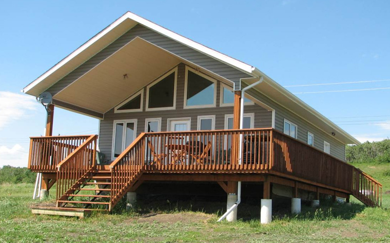 A house with a large deck sitting in a grass clearing with blue skies. This house is the What a View Cottage Rental.