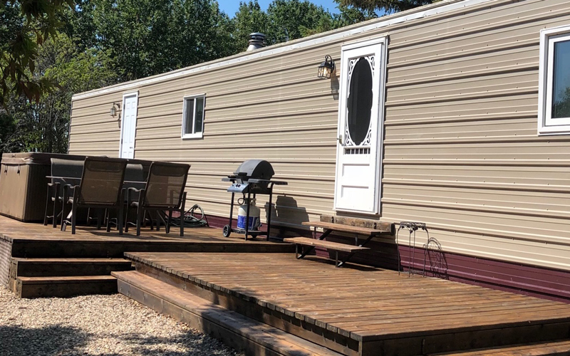 A brown trailer with a deck and hot tub outside.